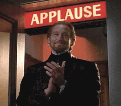 A Man In A Tuxedo Is Clapping In Front Of A Sign That Says Applause GIF