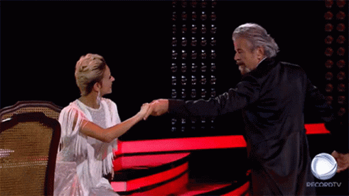 A Man In A Tuxedo Is Dancing With A Woman In A White Dress In Front Of A Sign That Says Recordtv GIF