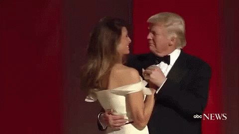 A Man In A Tuxedo Is Dancing With A Woman In A White Dress On A Red Carpet . GIF