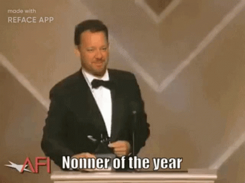 A Man In A Tuxedo Is Giving A Speech On A Stage In Front Of A Crowd And A Large Screen . GIF