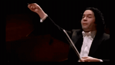 A Man In A Tuxedo Is Holding A Baton In Front Of A Green Bar With A Gold Coin On It GIF