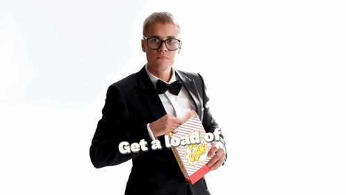 A Man In A Tuxedo Is Holding A Box Of Popcorn With The Words Get A Load Of This Guy Below Him GIF