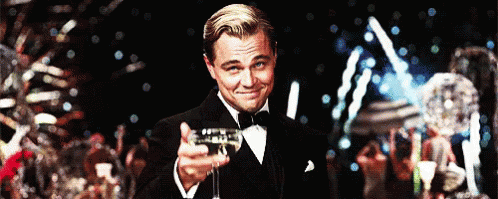 A Man In A Tuxedo Is Holding A Glass Of Champagne And Smiling GIF