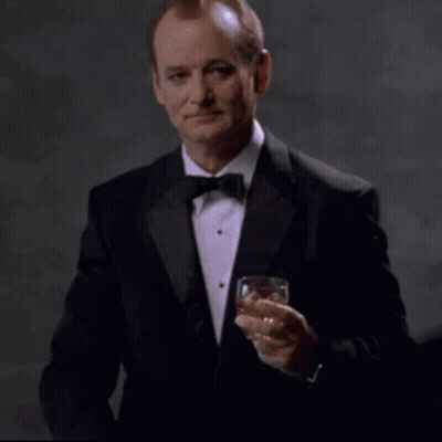 A Man In A Tuxedo Is Holding A Glass Of Whiskey And Pointing At The Camera With The Words You Da Man Above Him GIF