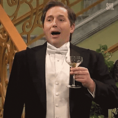 A Man In A Tuxedo Is Holding A Glass Of Wine In His Hand . GIF