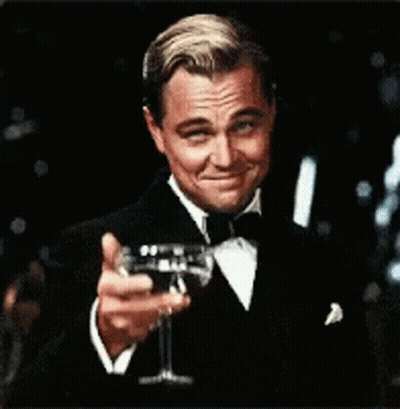 A Man In A Tuxedo Is Holding A Glass Of Wine In His Hand GIF