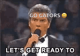 A Man In A Tuxedo Is Holding A Microphone And Saying `` Let 'S Get Ready To Go Gators '' GIF