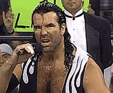 A Man In A Tuxedo Is Holding A Microphone In His Hand GIF