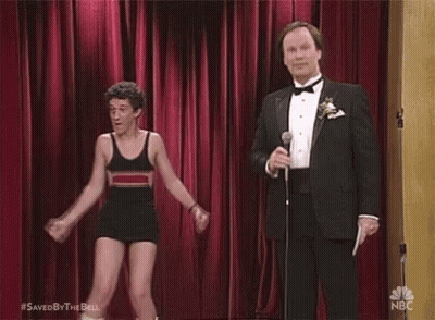 A Man In A Tuxedo Is Holding A Microphone While A Man In A Bathing Suit Is Dancing On Stage . GIF