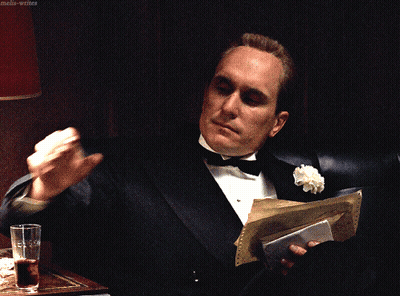 A Man In A Tuxedo Is Holding A Piece Of Paper And A Glass Of Water GIF