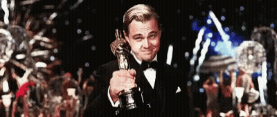 A Man In A Tuxedo Is Holding An Oscar In His Hand . GIF