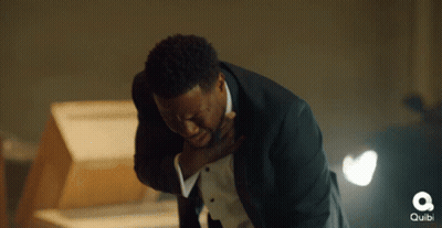 A Man In A Tuxedo Is Holding His Chest In Pain And The Word Quibi Is Visible In The Background GIF