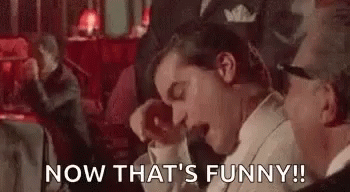 A Man In A Tuxedo Is Laughing With His Mouth Open While Sitting Next To Another Man . GIF