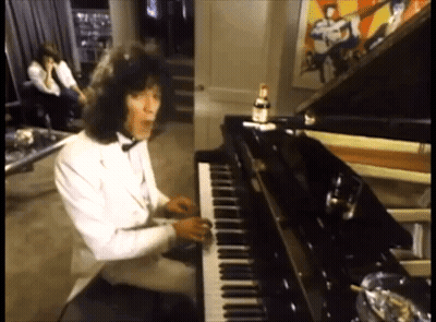 A Man In A Tuxedo Is Playing A Piano In A Room GIF