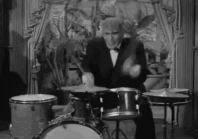 A Man In A Tuxedo Is Playing The Drums In A Black And White Photo . GIF