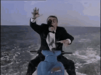 A Man In A Tuxedo Is Riding A Blue Scooter On Top Of A Mountain . GIF