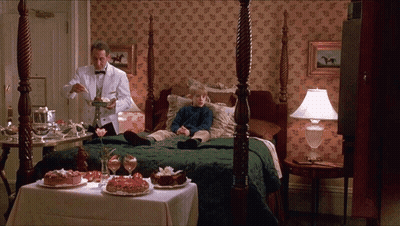 A Man In A Tuxedo Is Serving A Dessert To A Young Boy Laying On A Bed GIF