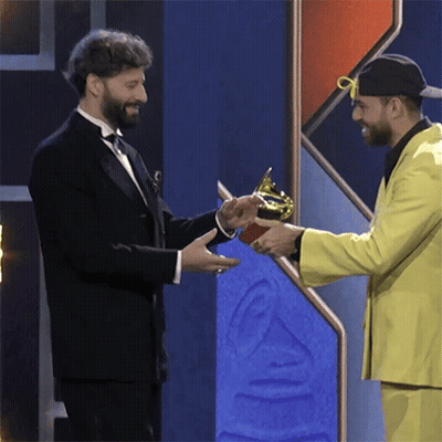 A Man In A Tuxedo Is Shaking Hands With Another Man In A Yellow Suit GIF