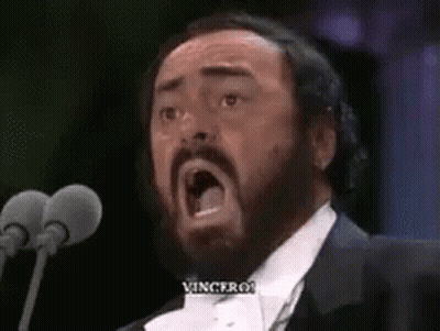 A Man In A Tuxedo Is Singing Into A Microphone With His Mouth Open . GIF