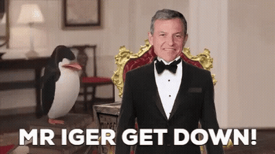 A Man In A Tuxedo Is Sitting In A Chair With The Words Mr Iger Get Down Behind Him GIF