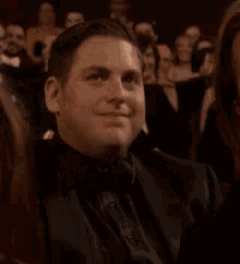 A Man In A Tuxedo Is Sitting In A Crowd Of People And Clapping . GIF