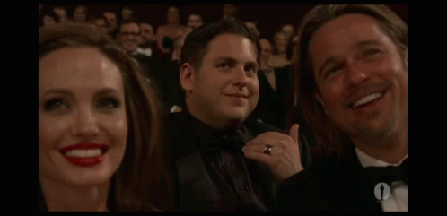 A Man In A Tuxedo Is Smiling In Front Of A Woman With Red Lips GIF