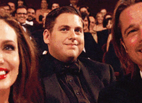 A Man In A Tuxedo Is Smiling While Sitting In A Crowd GIF