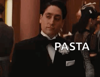 A Man In A Tuxedo Is Standing In A Room With The Word Pasta . GIF