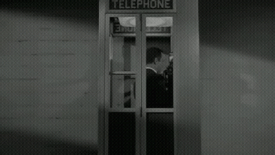 A Man In A Tuxedo Is Standing In A Telephone Booth In A Black And White Photo . GIF