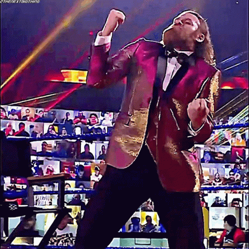 A Man In A Tuxedo Is Standing In A Wrestling Ring With His Arms In The Air . GIF