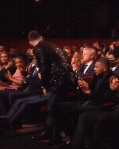 A Man In A Tuxedo Is Standing In Front Of A Crowd Applauding GIF