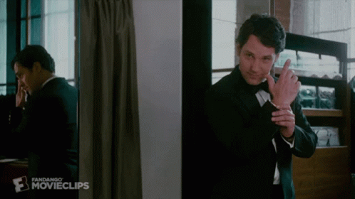 A Man In A Tuxedo Is Standing In Front Of A Mirror And Talking On A Cell Phone . GIF