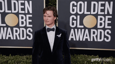 A Man In A Tuxedo Is Standing In Front Of A Sign That Says Golden Globe Awards GIF
