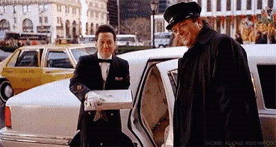 A Man In A Tuxedo Is Standing Next To A Man In A Limousine Holding A Box . GIF
