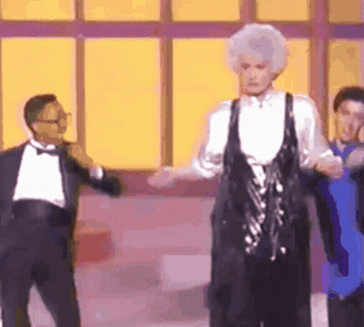 A Man In A Tuxedo Is Standing Next To A Woman In A Black Dress Who Is Dancing . GIF