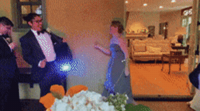 A Man In A Tuxedo Is Standing Next To A Woman In A Blue Dress In A Living Room GIF