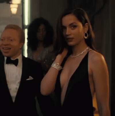 A Man In A Tuxedo Is Standing Next To A Woman In A Plunging Black Dress . GIF