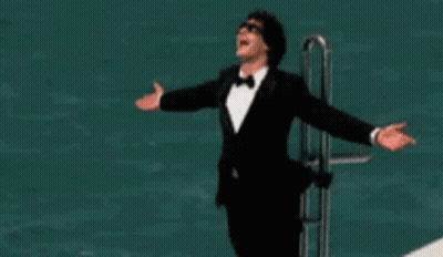 A Man In A Tuxedo Is Standing On A Boat With His Arms Outstretched . GIF