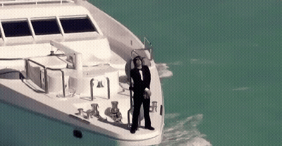 A Man In A Tuxedo Is Standing On The Side Of A Boat In The Ocean . GIF