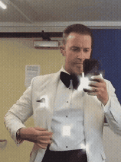A Man In A Tuxedo Is Taking A Picture Of Himself In A Mirror GIF