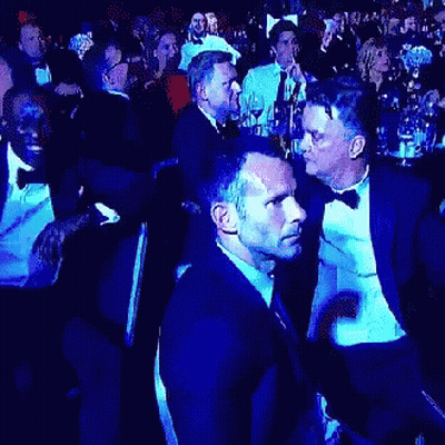 A Man In A Tuxedo Is Talking To Another Man In A Crowd Of People GIF
