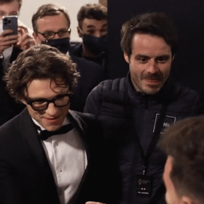 A Man In A Tuxedo Is Talking To Another Man In A Jacket With Mh On It GIF