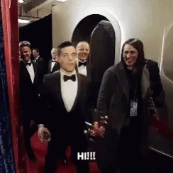 A Man In A Tuxedo Is Walking Down A Red Carpet With A Woman Behind Him . GIF