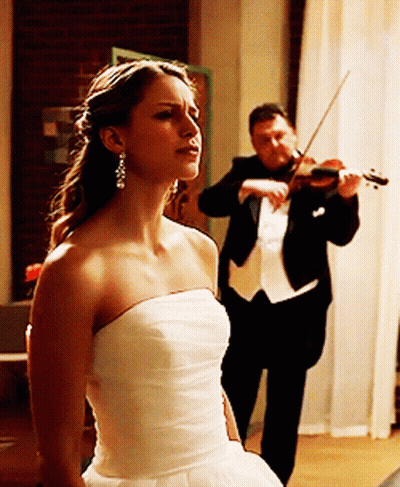 A Man In A Tuxedo Plays A Violin While A Woman In A White Dress Looks On GIF