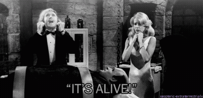 A Man In A Tuxedo Says " It 'S Alive " In Front Of A Woman In A White Dress GIF