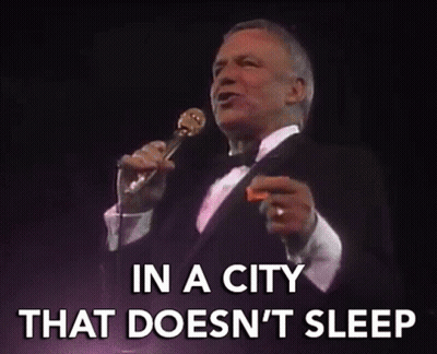 A Man In A Tuxedo Singing Into A Microphone With The Words In A City That Does N't Sleep GIF