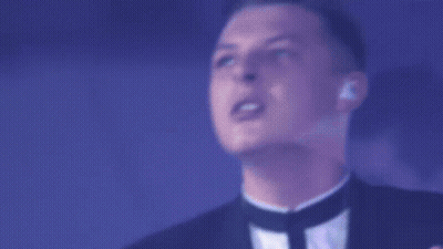 A Man In A Tuxedo Sings Into A Microphone In Front Of A Drum Set That Has The Letter N On It GIF
