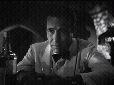 A Man In A Tuxedo Sits At A Table With A Glass And A Bottle Of Alcohol GIF