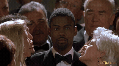 A Man In A Tuxedo Stands In A Crowd Of People With The Word Bounce On The Bottom Left GIF