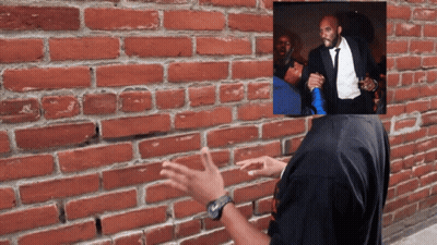 A Man In A Tuxedo Stands In Front Of A Brick Wall With His Hands Outstretched GIF